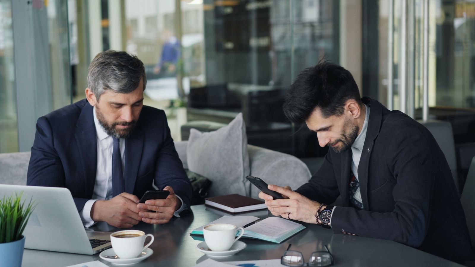 Two professionals using smartphones at a cafe table